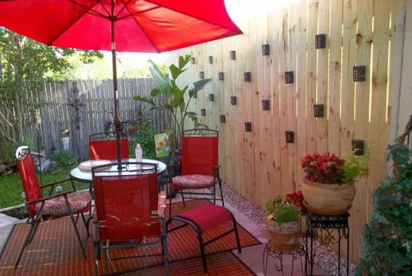 Gartenzaun Gartengestaltung Gartensichtschutz rote Gartenmöbel Sitzecke mit rotem Sonnenschirm 