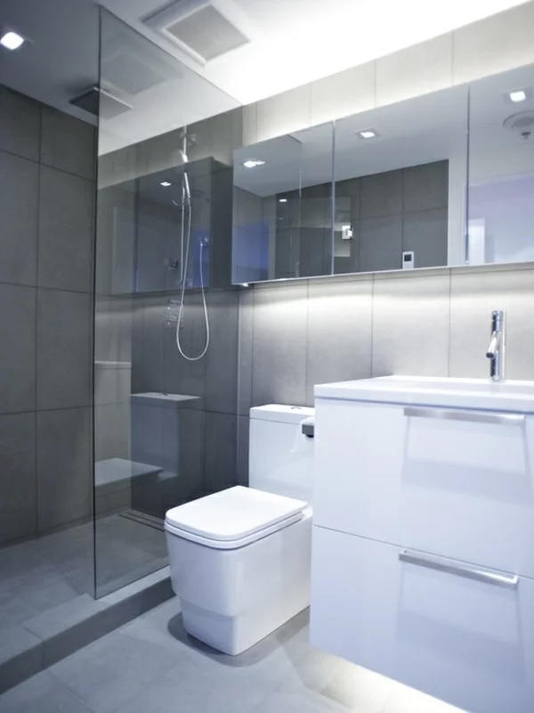 kleines Bad planen im minimalistischen Stil gestalten Dusche Glaswand weiße Badmöbel eingebaute Raumbeleuchtung 