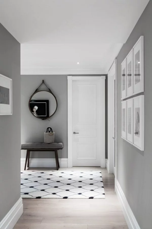 helle Gestaltung im Flur Wandfarbe grau weiße Tür runder Wandspiegel gemusterter Teppich Bildwand rechts 