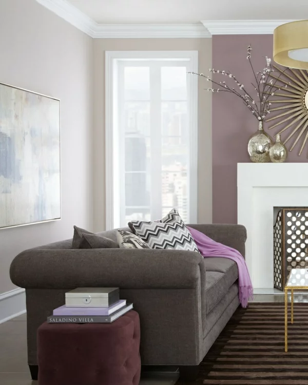 Wandfarbe hellgrau im Wohzimmer mit rosa und lila Akzenten dazu dunkles Sofa Kamin und lila Wurfdecke