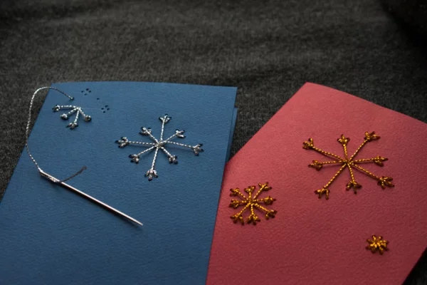 Weihnachtsbastelideen Weihnachtskarten basteln mit Schneeflöckchen aus glänzenden Fäden auf Buntpapier