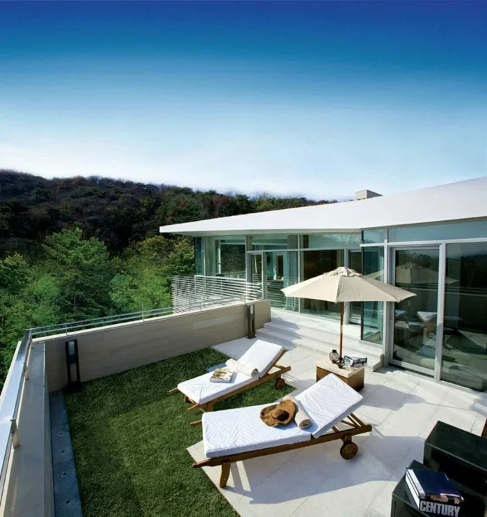 moderne Terrassen Ideen moderner Stil bequeme weiße Liegesessel Sonnenschirm grüner Rasen