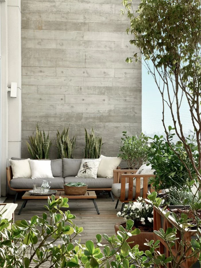 moderne Stadtwohnung zahlreiche Topfpflanzen bequeme Balkonmöbel aus Holz mit grauer Polsterung gemütliche Sitzecke 