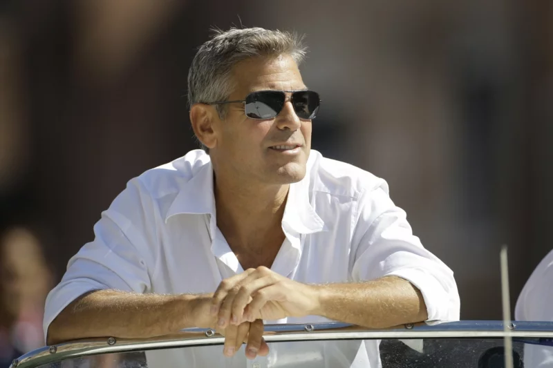 Hollywood Schauspieler über 50 George Clooney auf einer Terrasse mit Sonnenbrille im weißen Hemd 