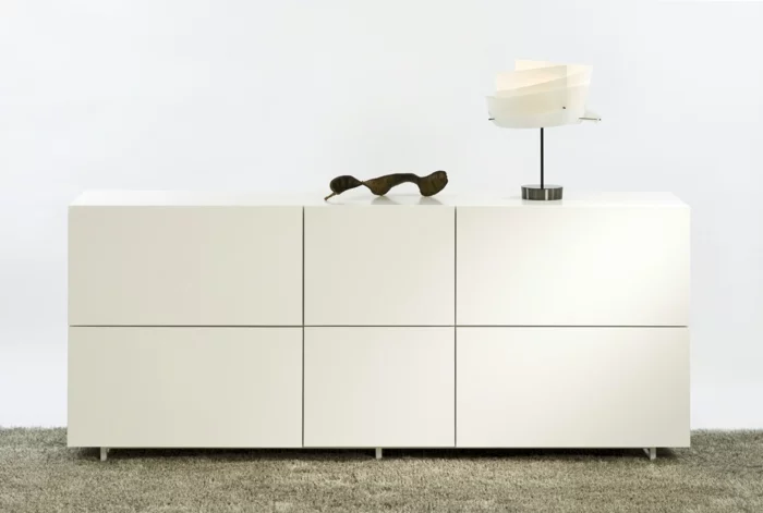 minimalistische, weiße Kommode mit Tischlampe und abstrakter Deko 