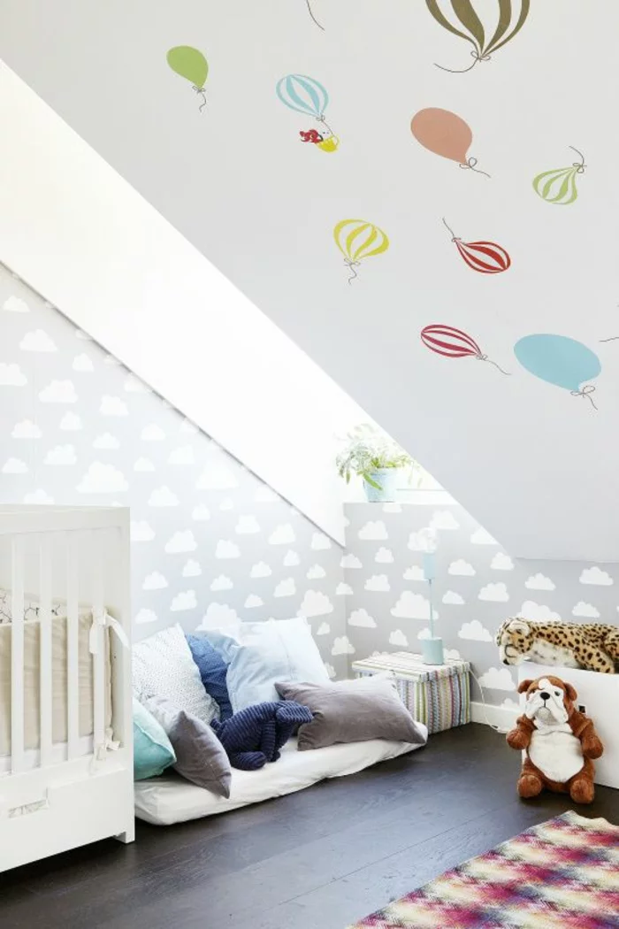 sehr kleines Babyzimmer mit Dachschräge eingerichtet mit Babybett, vielen Kissen und Wandtattoos Heißluftballons