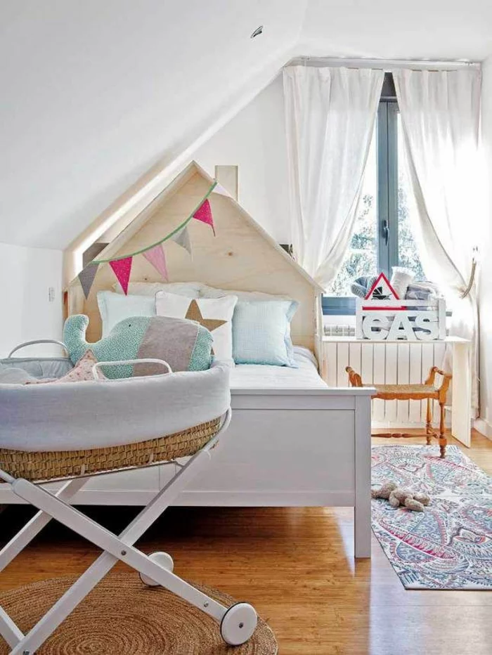 Kinderzimmer mit Dachschräge mit weißem Bett mit DIY Kopfteil und Babykorb