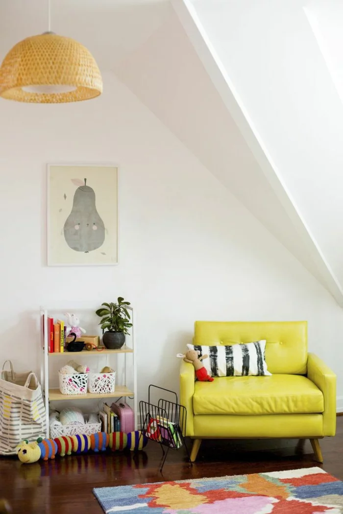 Kinderzimmer mit Dachschräge mit gelbem Mini-Sofa, buntem Kinderteppich, kleinem Regal und Hängeleuchte aus Bambus