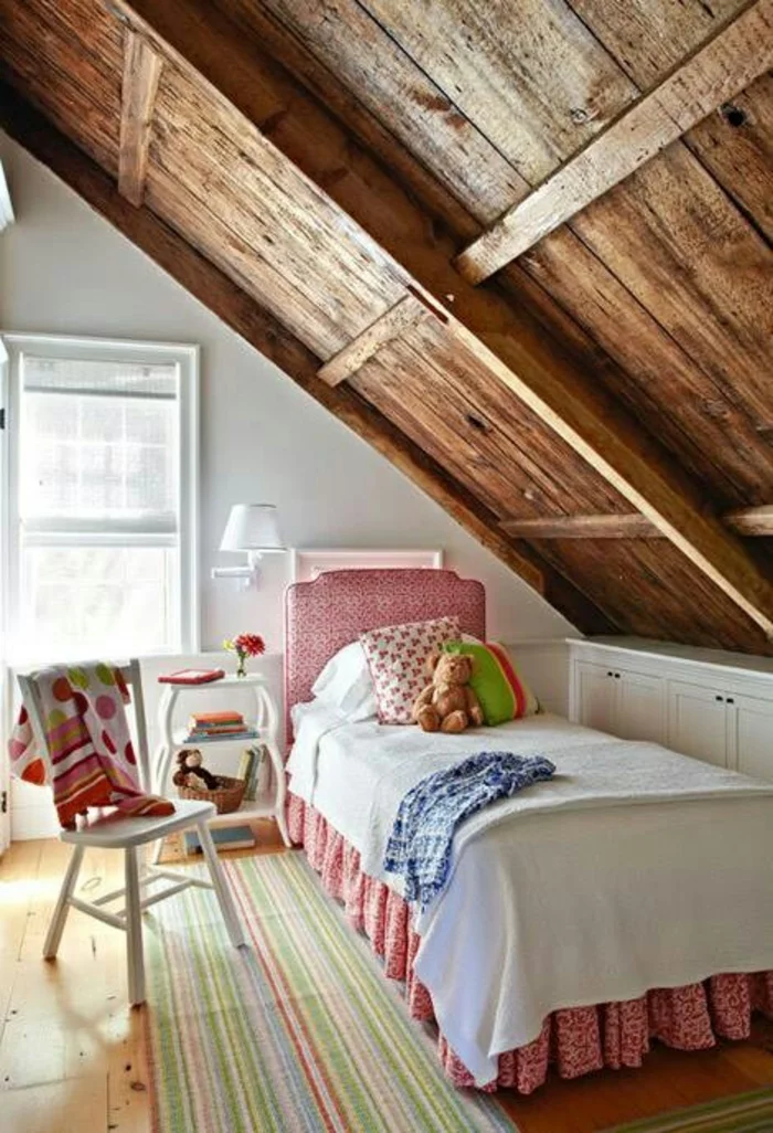 Kinderzimmer mit Dachschräge aus dicken Holzbalken, gestreiftem Teppich und großem Fenster 