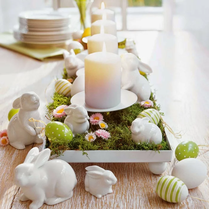 Tischdeko mit Porzellan-Hasen, Moos, Gänseblümchen und weißen Stumpenkerzen 