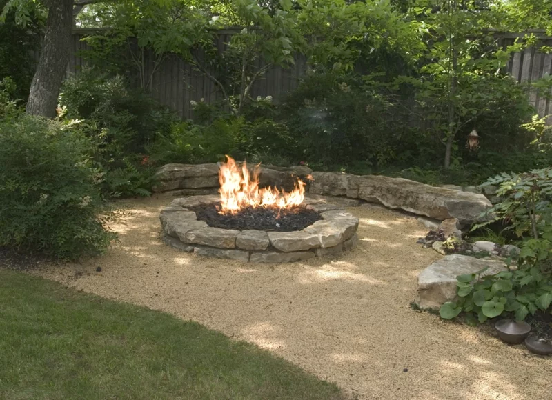Feuerstelle bauen aus Stein Gartengestaltung Boden aus Kies Sand üppiges Grün ringsum