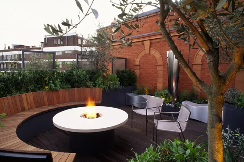 Feuerstelle bauen moderne Gartengestaltung Tisch mit eingebautem Kamin weiße Stühle