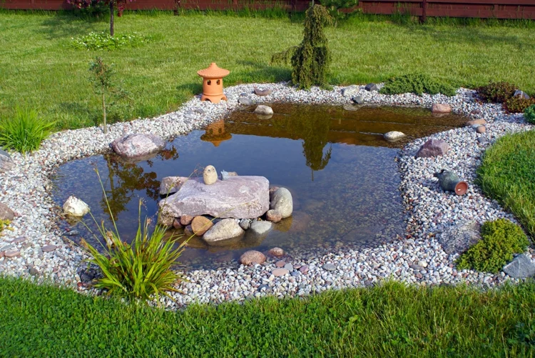 Gartenteich anlegen mit Steinen in runder Form Steine im Wasser Gestaltung mit Kies grüner Rasen 