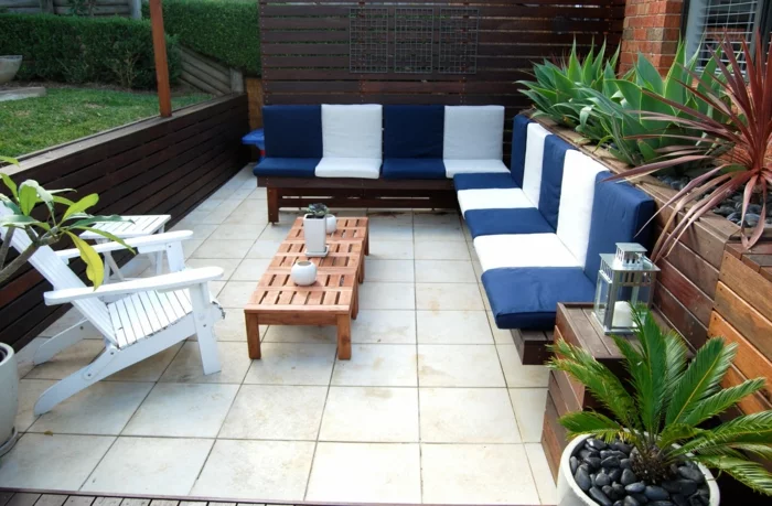Sitzecke mit Gartensofa mit Dekokissen in Weiß und Blau und Bodenfliesen