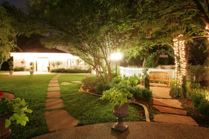 Gartengestaltung mit zwei Gartenwegen aus Gehwegplatten und romantischer Beleuchtung