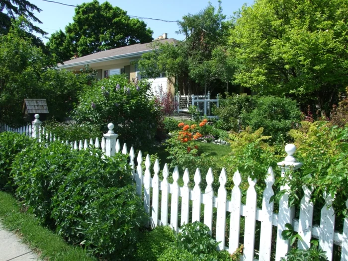 Hinterhof mit vielen Pflanzen und einem weißen Holzzaun