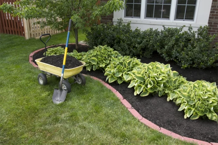 Gartengestaltung - Beeteinfassung mit Steinen und grüne Gartensträucher
