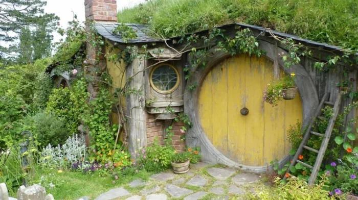 kleines Hobbit Gartenhaus aus Holz und Ziegeln, umgeben von vielen Pflanzen 