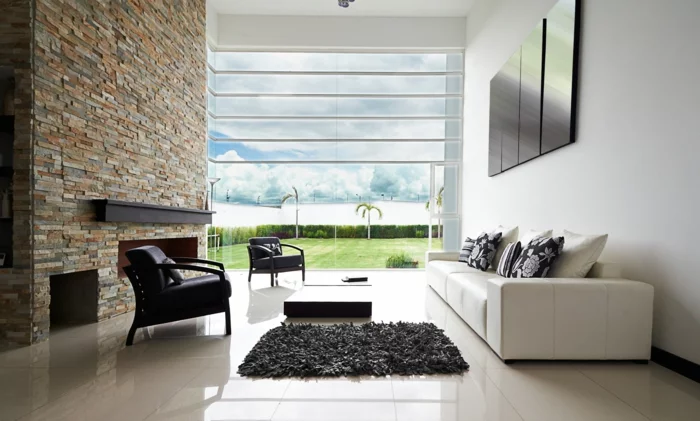 Steinwand im Wohnzimmer, moderne Feuerstelle, weißes Sofa und Panoramafenster
