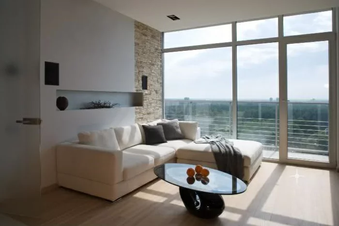 Steinwand im Wohnzimmer, Panoramafenster, beiges Sofa und heller Boden