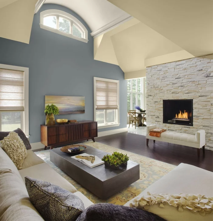 Wohnzimmer mit Steinwand, blauer Akzentwand, Kamin und hellgelber Decke