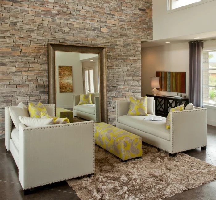 Wohnzimmer mit Steinwand, beigen Sofas und einem großen Spiegel