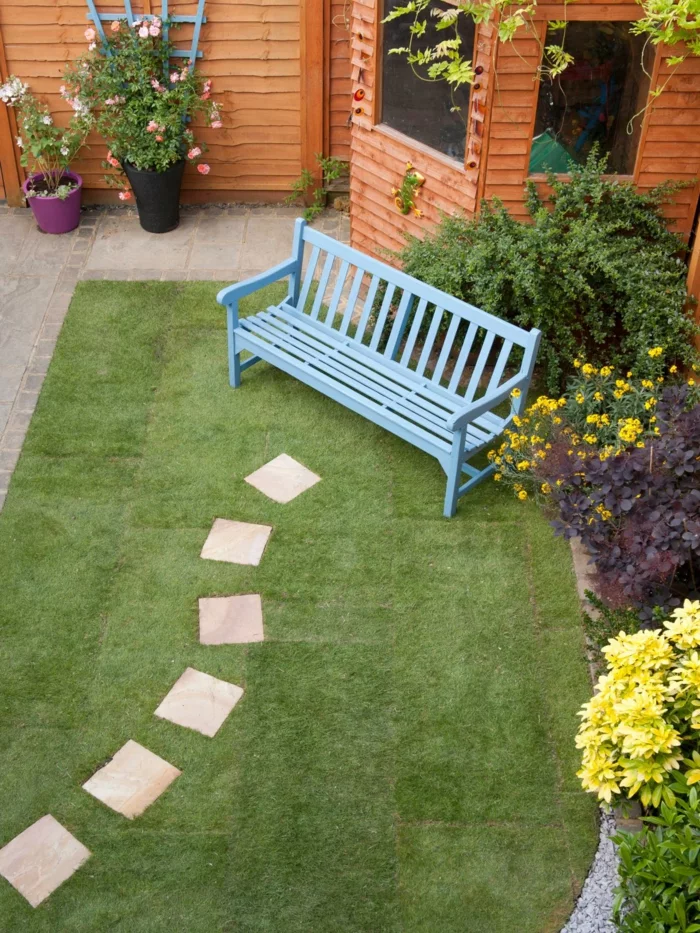 Gartenwege gestalten - Gehwegplatten, blaue Sitzbank und grüner Rasen