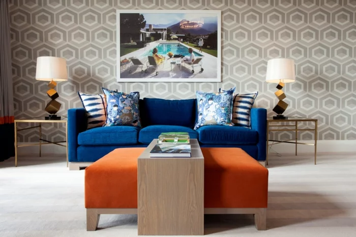 blaues Sofa, oranger Hocker und gemusterte Wandtapete