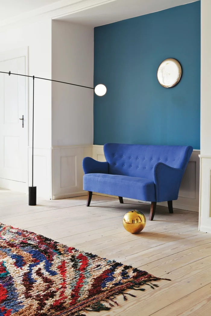 Holzboden, blaues Sofa mit Retro Design und grüne Wand