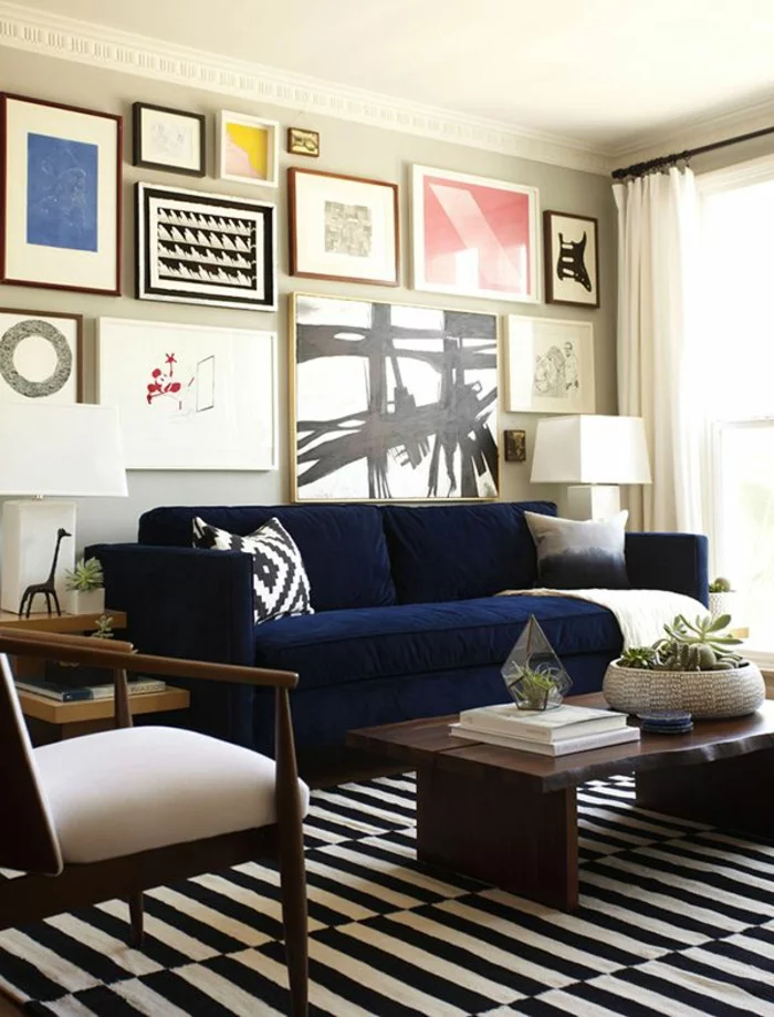 kleines Wohnzimmer mit Streifenteppich, Sofa in Blau und vielen Wandbildern 