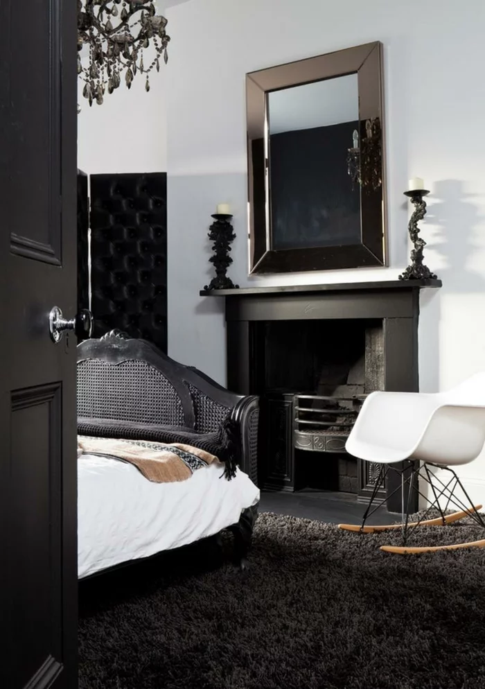 modernes Schlafzimmer mit schwarzer Trennwand, dunklem Teppich und weißem Schaukelstuhl
