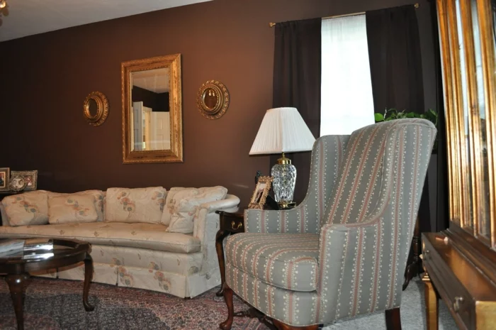 kleines Wohnzimmer mit braunen Wänden, Wandspiegel und Sofa mit einem floralen Muster