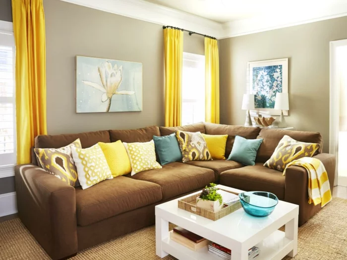 kleines Wohnzimmer mit braunem Sofa, weißem Couchtisch und gelben Gardinen