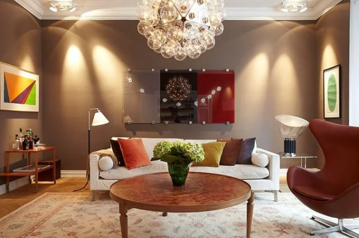 Wohnzimmer in Braun mit einem Ohrsessel, Leuchter und modernen Wandbildern