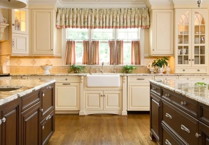 cremefarbene Küchenschränke, braune Kücheninsel, Boden in Holzoptik und kurze Gardinen