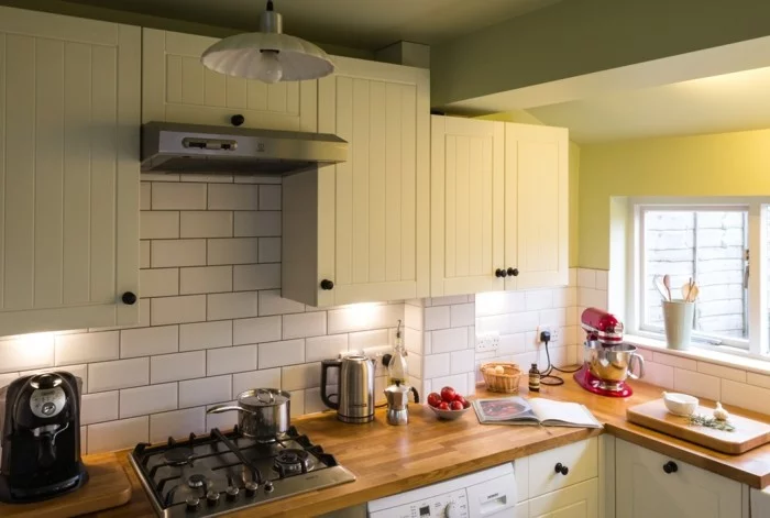moderne kleine Küche mit weißen Metro Fliesen, Oberschränken in Creme und hölzerner Arbeitsoberfläche