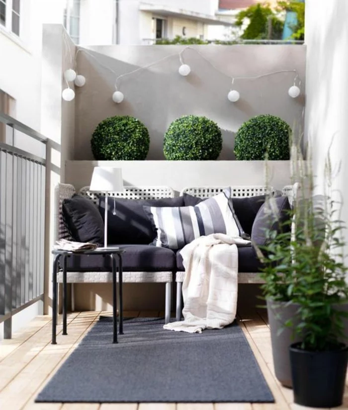 balkon gestalten balkonmöbel rattanmöbel sofa sitzbank hocker beistelltisch lichterkette buchsbaum holzdielen