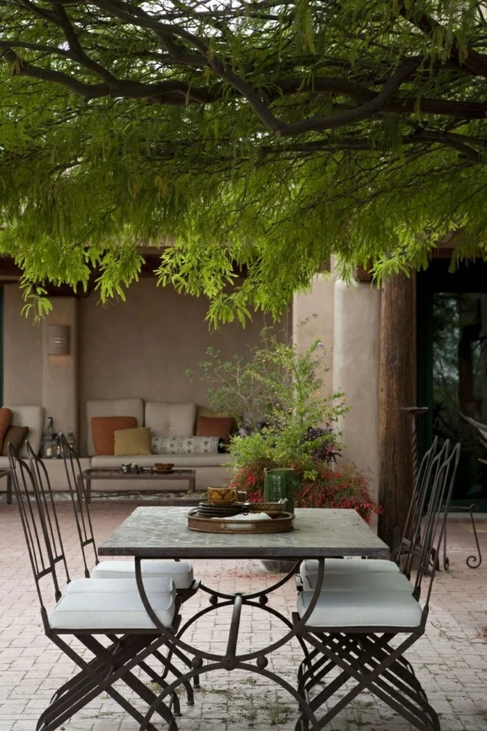 mediterrane Gartengestaltung mit einem stilvollen Essbereich unter einem großen Baum