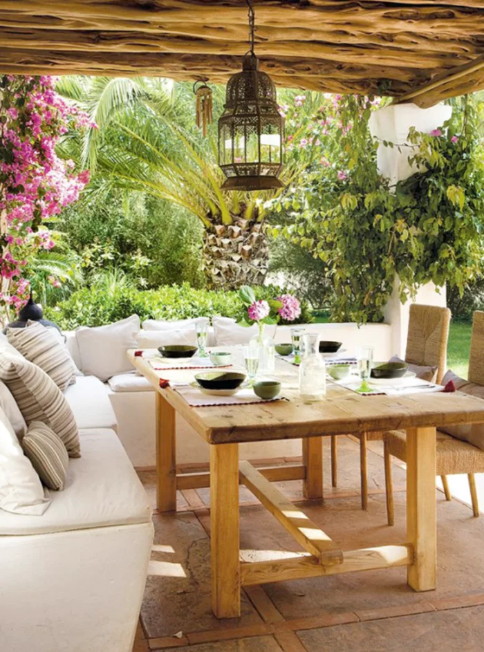 mediterrane Gartengestaltung mit Holztisch, weißen Gartensofas und einer schönen Hängelampe