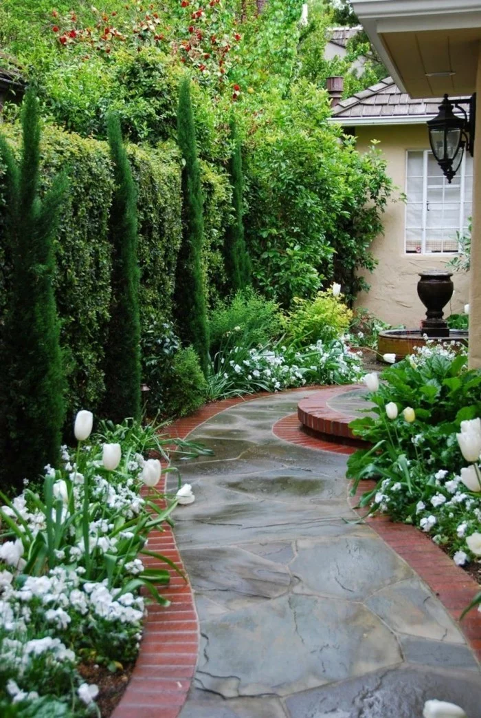 Gartenweg aus Stein, Zypresse als Sichtschutz und Gartenblumen mit weißen Blüten