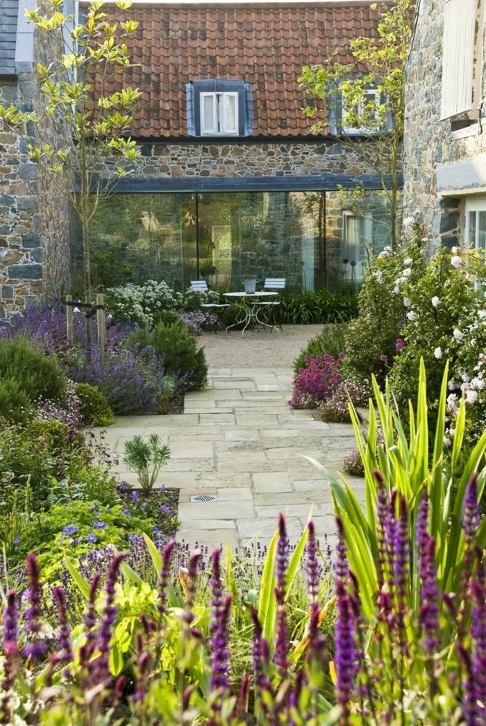 mediterrane Gartengestaltung mit Lavendel, vielen Gartensträuchern, Steinboden und kleinem Gartentisch