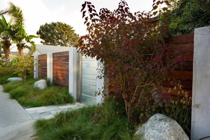 moderner Holzzaun und schöner Vorgarten mit Steinen und Gräsern