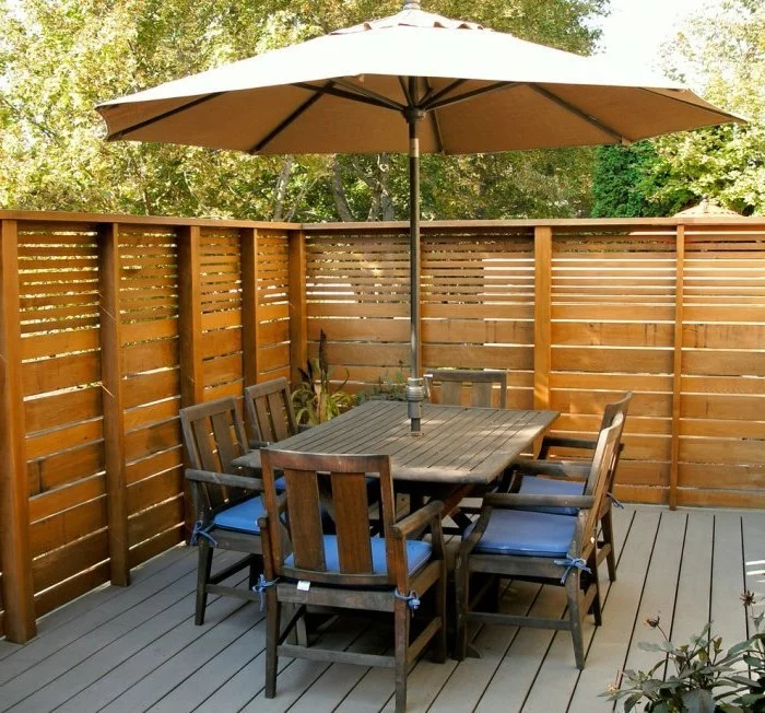 Holzzaun, großer Gartentisch und Sonnenschirm