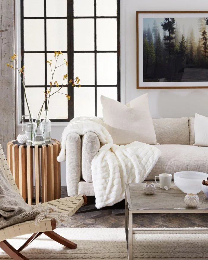 Hygge Stil im Wohnzimmer durch weiße Decken, Dekokissen und Holzelementen