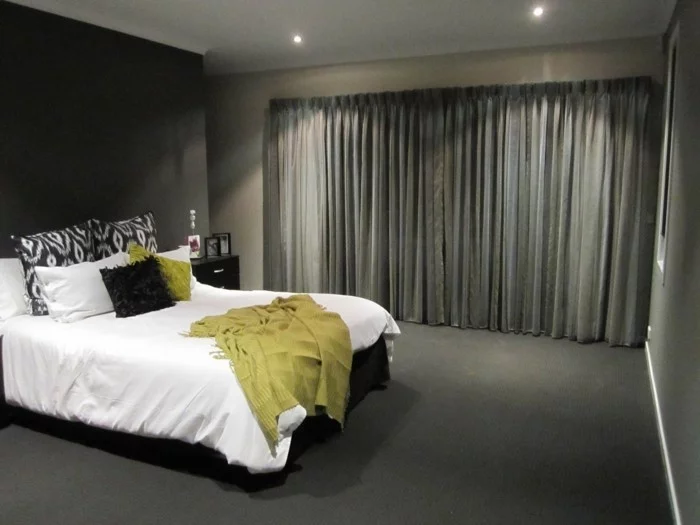 Schlafzimmer Gardinen in Dunkelgrau und dunkler Teppichboden machen einen Kontrast zur weißen Bettwäsche
