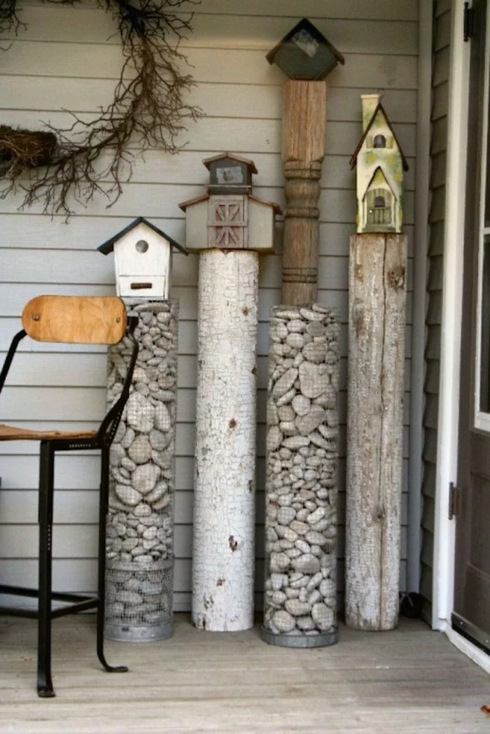 Steine in kleinen Metallkörben und Holzstämme mit Vogelhäusern dekoriert