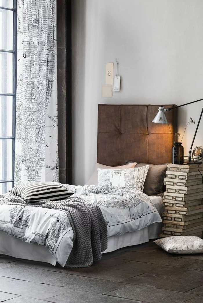 Gardinen mit einem ausgefallenen Muster, helle Bettwäsche, Bodenfliesen und origineller Nachttisch