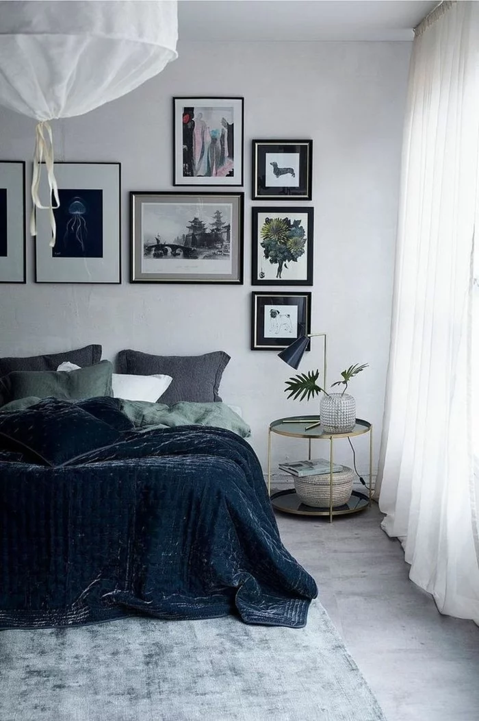 Schlafzimmer mit weißen transparenten Gardinen, dunkler Bettwäsche und vielen Wandbildern