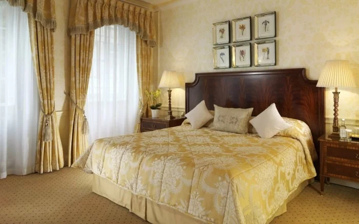 luxuriöses Schlafzimmer mit eleganten Vorhängen in Gold, zur Seite gebunden, und weiße transparente Gardinen