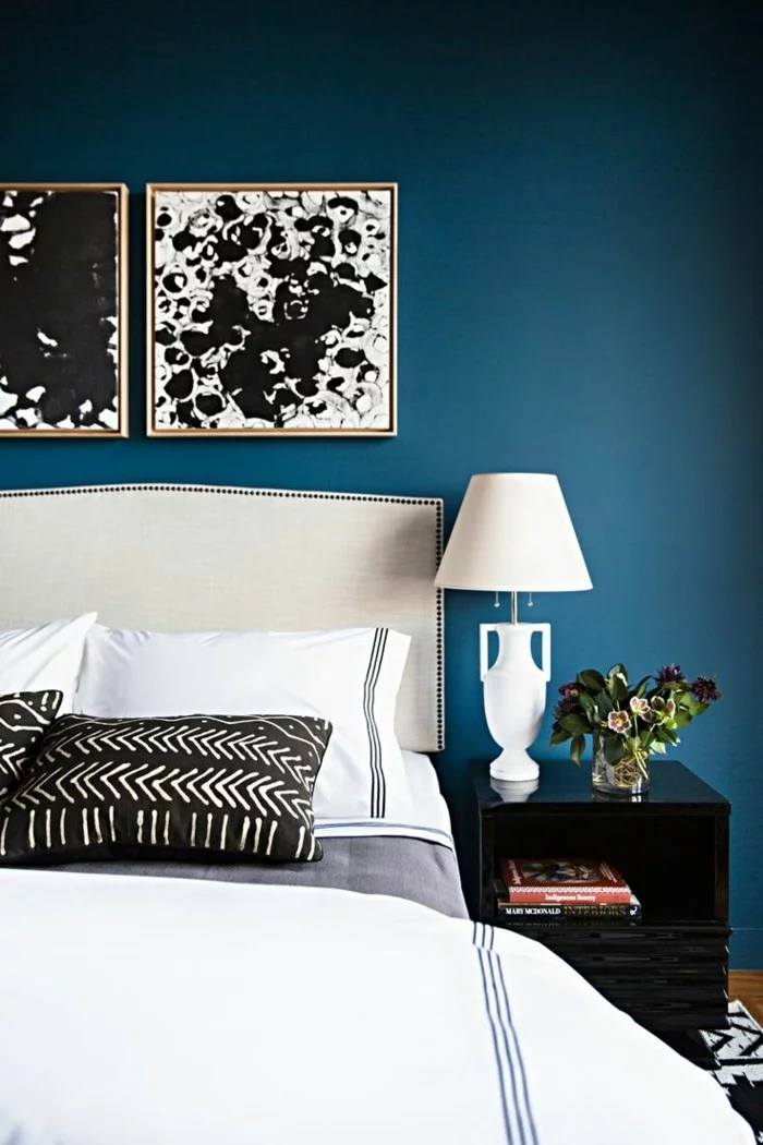 Schlafzimmer mit weißer Bettwäsche, abstrakten Wandbildern und Wandfarbe Petrol 